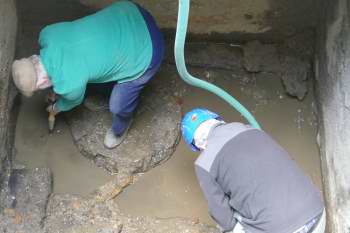 2 men working at the bottom of a large muddy pit