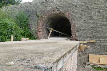 Looking along   a concrete slab towards a brick arched hole in a stone wall