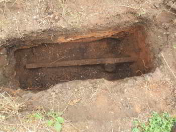 Open pit surrounded by soil with a rusty rail at the bottom