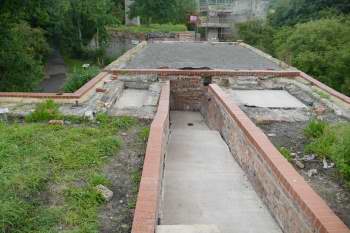 a brick channel with a concrete floor leads to a flat roofed building