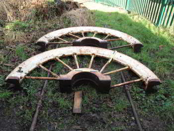 Two white painted half wheels sit on a grassy area.  Their rims are connected to the central hub by thin spokes.